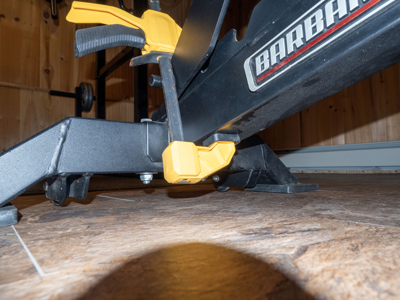 Photo of Barbarian Line heavy duty weight bench with trigger clamp foot resting on bottom rail to secure the bench for vertical storage. Picture five.
